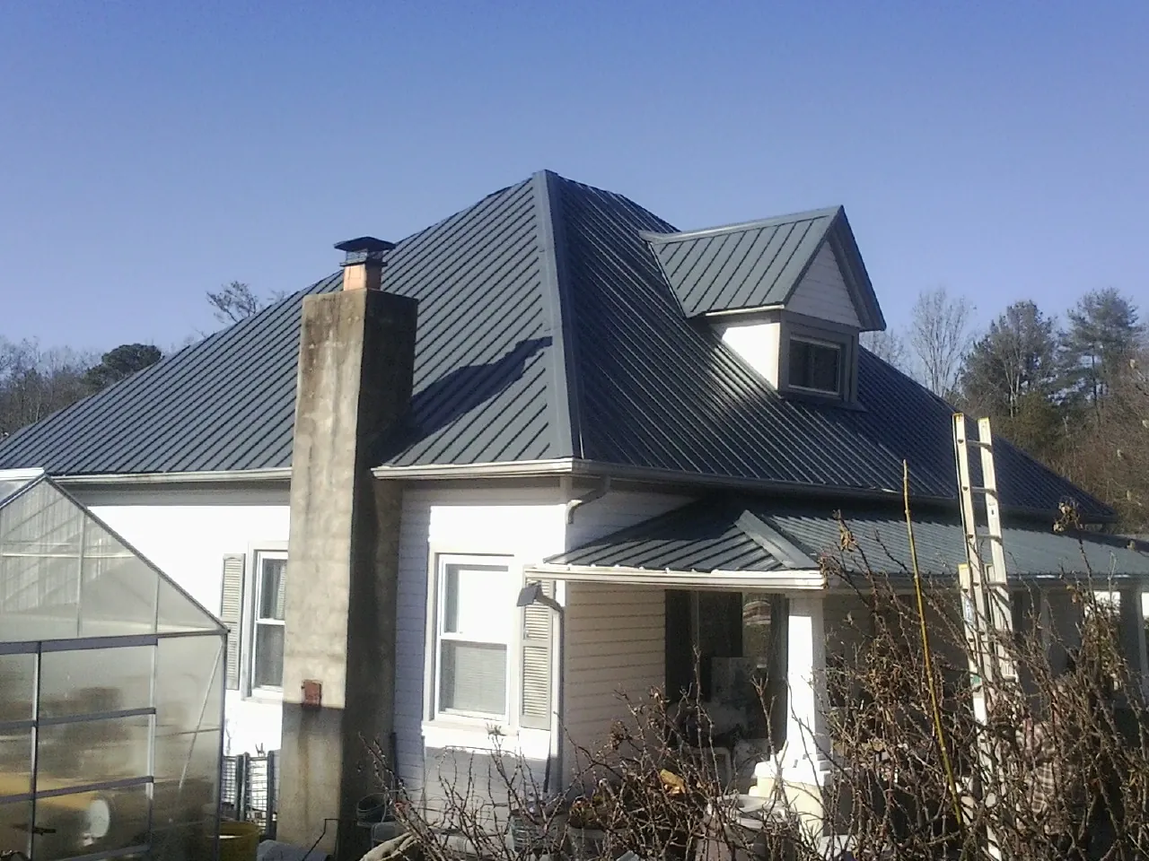 Dark blue standing seam metal roof on a white farmhouse with dormer — Slate & Tile Roof Repair by Roofing Brothers in Pine Ridge