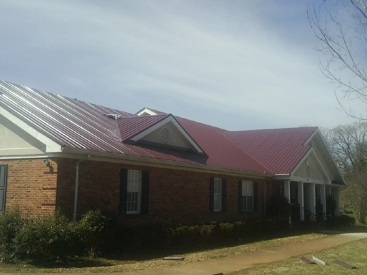 Red metal roof with gabled entries on a long brick building, from a Hail Damage Roof Repair job in Pine Ridge