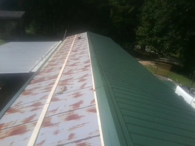 Old rusted panels beside newly installed green metal roofing — Wind Damage Roof Repair by Roofing Brothers in Pine Ridge