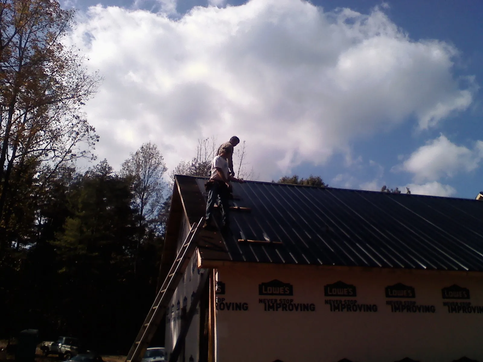 Roofer fastening dark metal panels high against a cloudy sky, from a Roof Inspection job in Pine Ridge