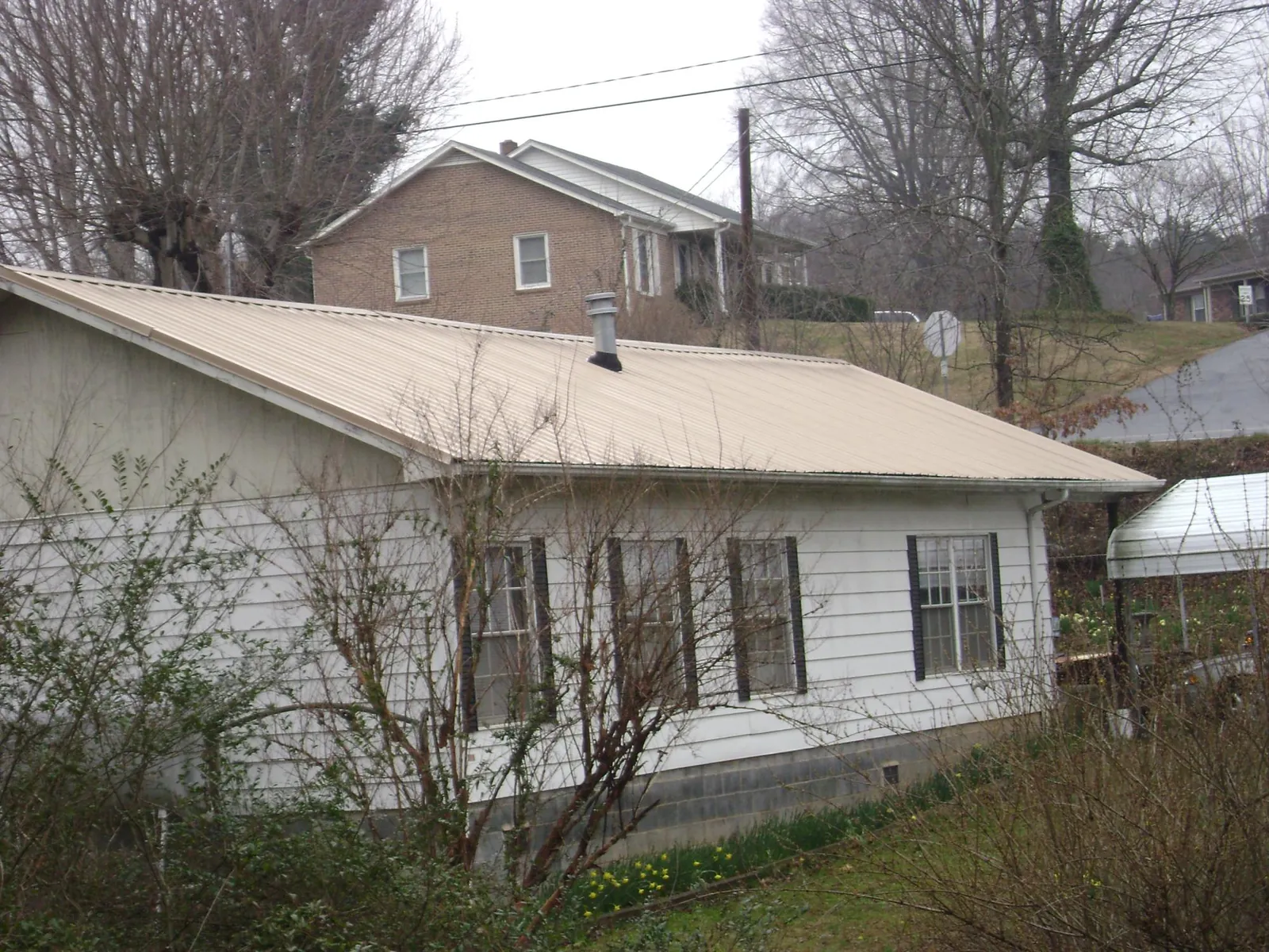 Tan metal roof on a white sided house set into a hillside — Commercial Roofing by Roofing Brothers in Pine Ridge
