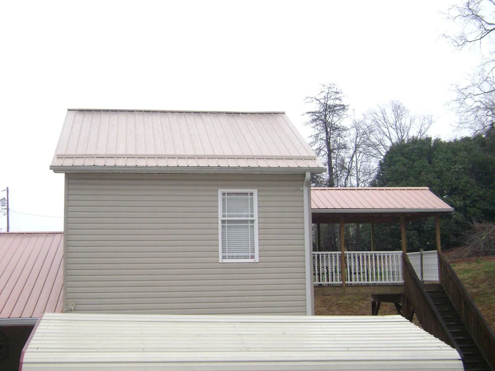 Tan metal roofs on a two story addition and attached porch, from a Roof Replacement job in Pine Ridge